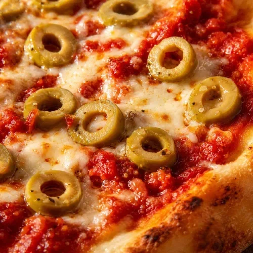 Close-up of sliced green olives on melted mozzarella cheese and tomato sauce on pizza.