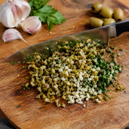 Hand chopped green olive tapenade recipe on wooden board using knife garlic and herbs for rustic olive spread